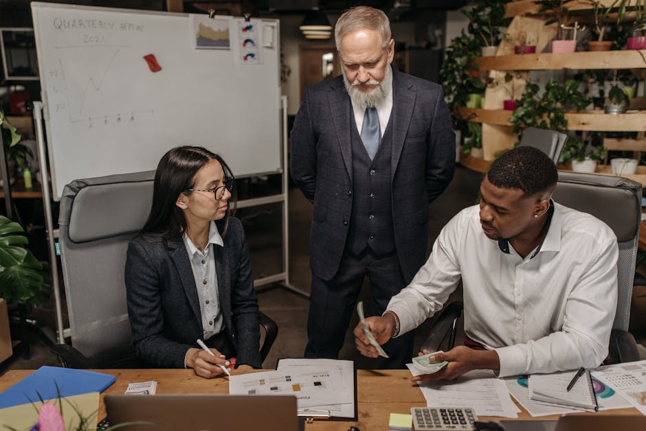 Three business professionals discussing reports at an office desk.